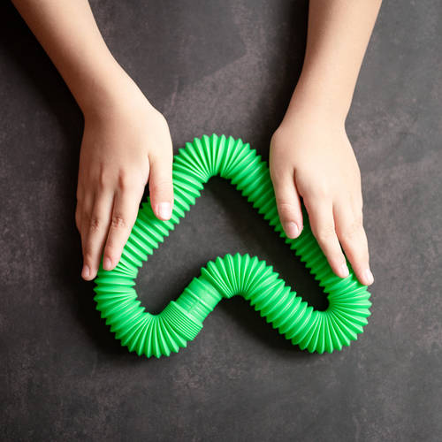 anti stress sensory pop tube toys in a children’s hands. a little happy kids plays with a poptube toy on a black table. toddlers holding and playing pop tubes green bright color, trend 2021 year