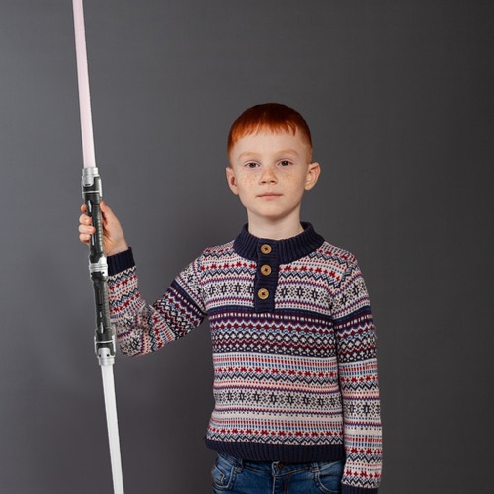 A little boy poses with a sword in a studio on a gray background.